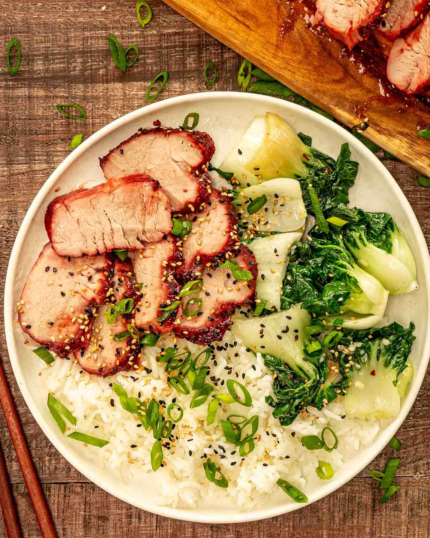 Beautifully glazed char siu pork sliced and arranged on a white platter with garnish of green onions and sesame seeds