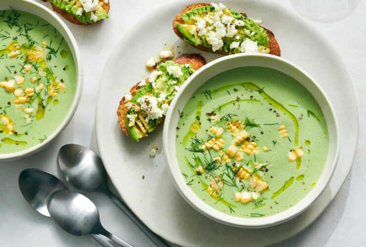 Cold Cucumber Avocado Soup No Cook Recipe - Fresh Summer Nutrition in 10 Minutes 27 Elegant bowl of pale green cold cucumber avocado soup garnished with fresh herbs, cucumber slices, and a drizzle of olive oil, served on a light wooden board with crusty bread