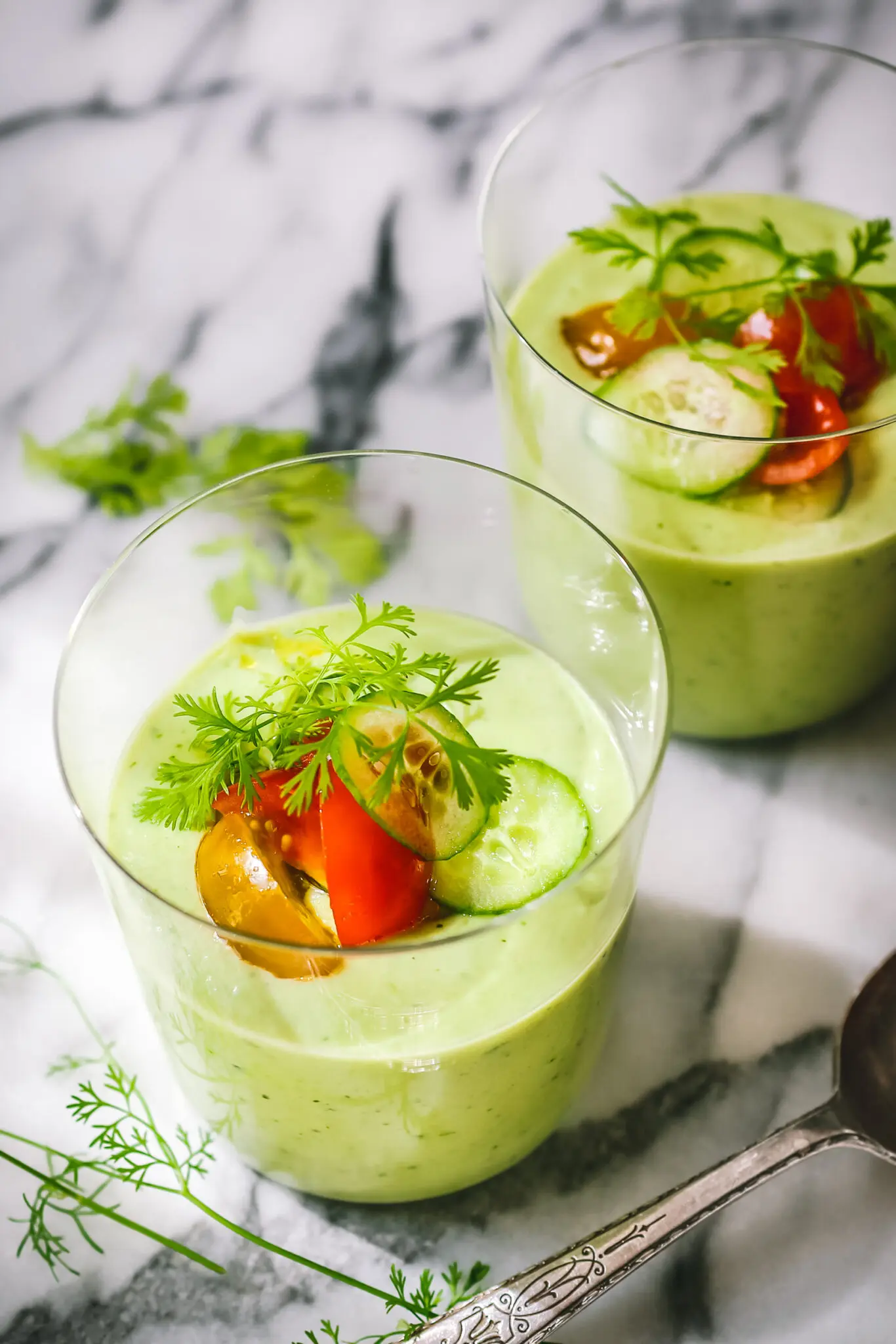 Cold Cucumber Avocado Soup No Cook Recipe - Fresh Summer Nutrition in 10 Minutes 27 Fresh ingredients laid out on a marble counter - whole cucumbers, halved avocados, fresh herbs, lime, and a high-speed blender in the background