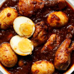 Ethiopian Doro Wat served in a traditional clay pot with hard-boiled eggs, garnished with fresh herbs, alongside injera bread