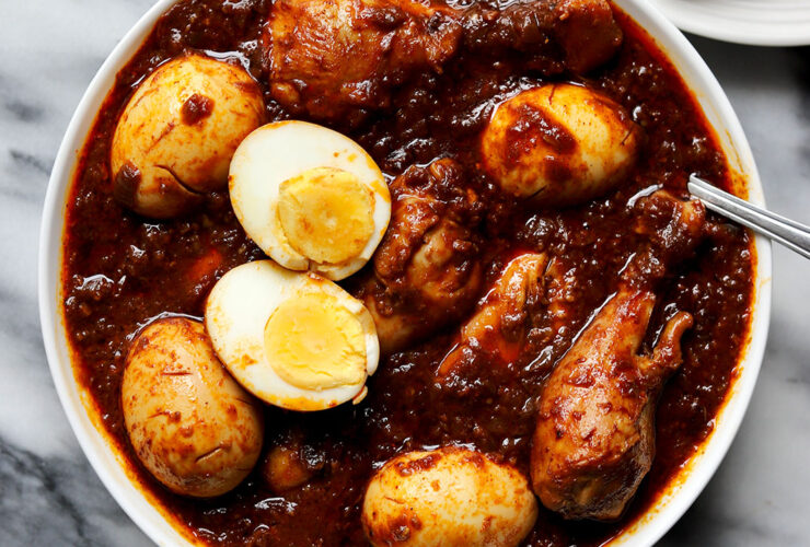 Ethiopian Doro Wat served in a traditional clay pot with hard-boiled eggs, garnished with fresh herbs, alongside injera bread