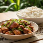 Filipino chicken adobo served in a white bowl with steamed rice, garnished with fresh cilantro and sliced green onions, shot from above on a rustic wooden table