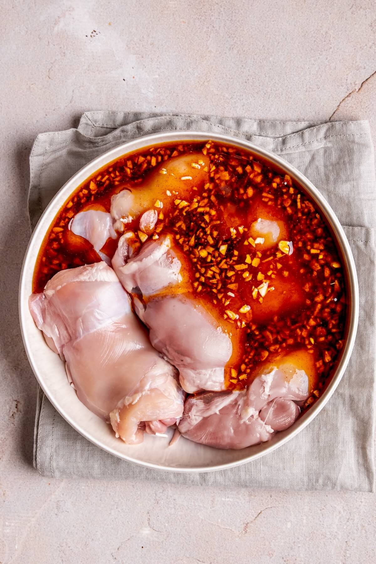 Raw chicken thighs, garlic cloves, bay leaves, and bottles of soy sauce and vinegar arranged on a marble cutting board