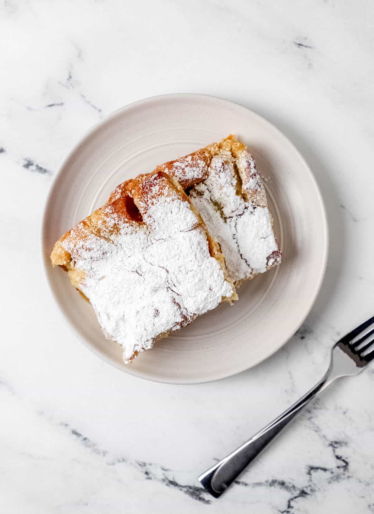 French Toast Casserole - Make-Ahead Breakfast with Clean Ingredients & Nutritional Benefits 28 Close-up slice of French toast casserole on white plate with fork, showing custardy interior and golden top, garnished with fresh berries and mint