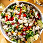 Colorful shrimp ceviche served in a white bowl garnished with cilantro and avocado slices, with lime wedges on the side