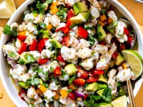Colorful shrimp ceviche served in a white bowl garnished with cilantro and avocado slices, with lime wedges on the side
