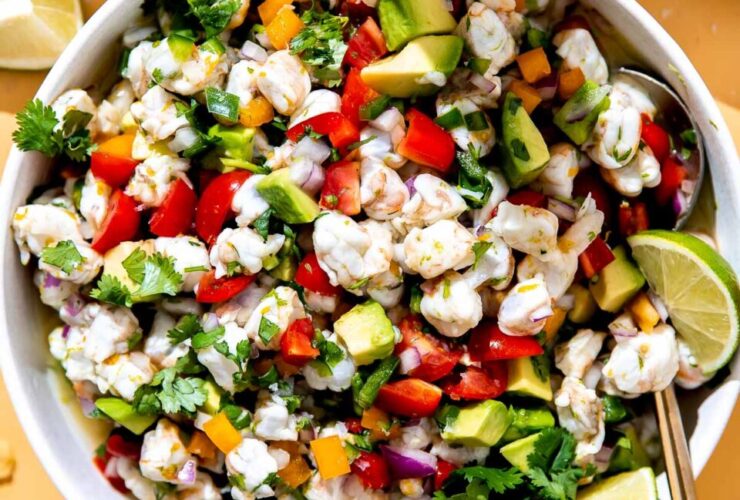 Colorful shrimp ceviche served in a white bowl garnished with cilantro and avocado slices, with lime wedges on the side
