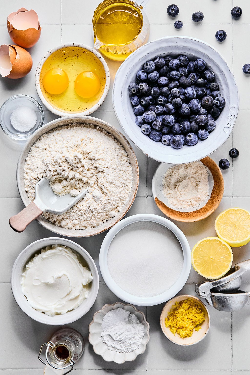 A step-by-step flat lay showing a bowl of fresh blueberries, a bowl of Greek yogurt, a fork for dipping, and a parchment-lined baking sheet ready to go into the freezer