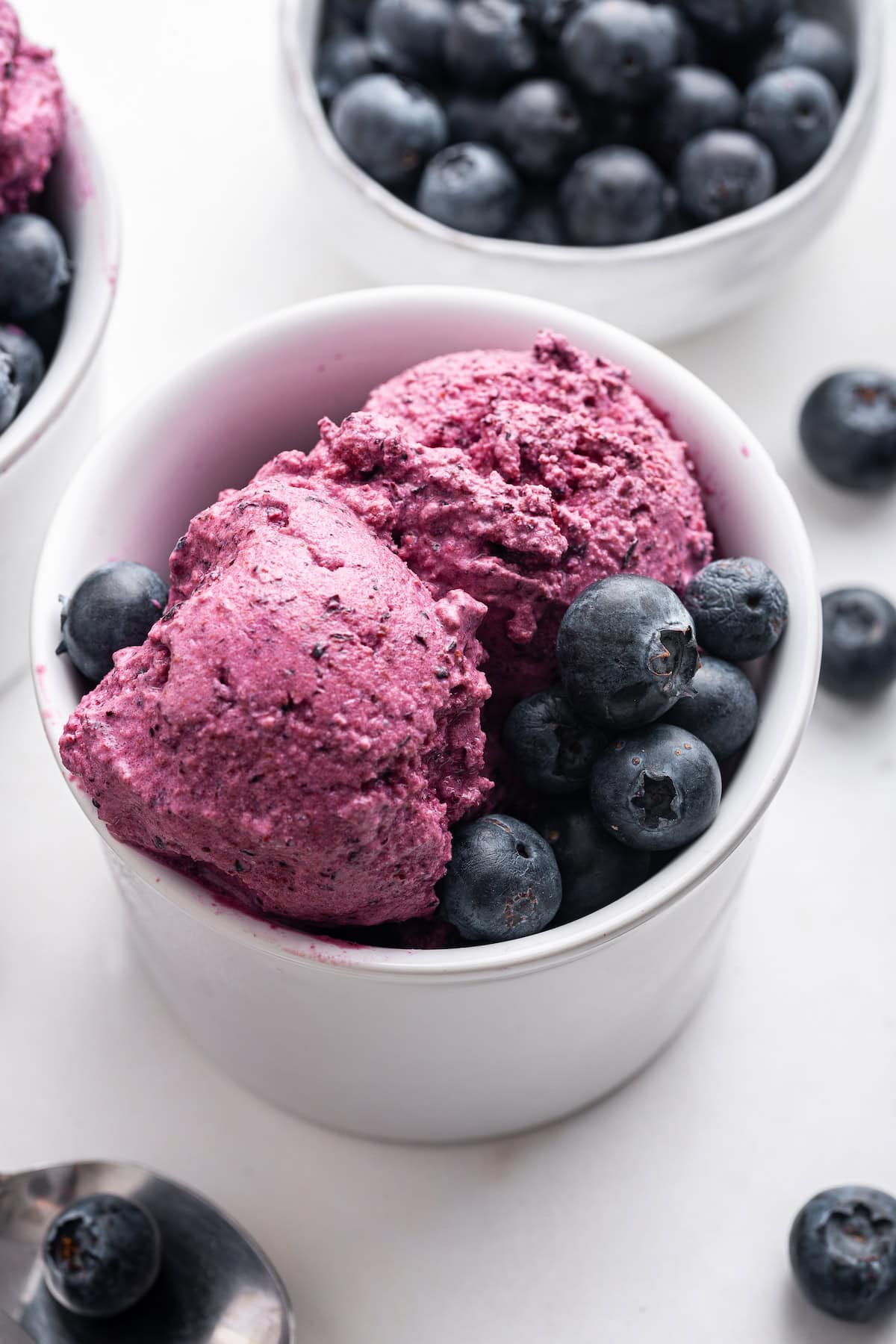 A close-up macro shot of frozen yogurt covered blueberries in a small ceramic bowl, with the frosty yogurt coating visible and a few berries split open to show the fresh fruit inside