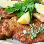 Golden German schnitzel cutlets plated elegantly with lemon wedges and fresh herbs on a white ceramic plate