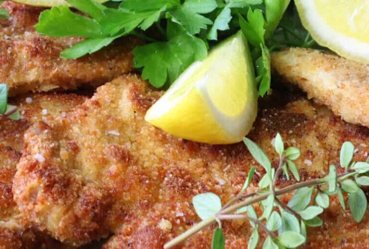 Golden German schnitzel cutlets plated elegantly with lemon wedges and fresh herbs on a white ceramic plate