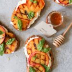 Grilled peach and burrata toast on whole grain bread beautifully plated on rustic wooden board with fresh basil garnish and drizzle of honey