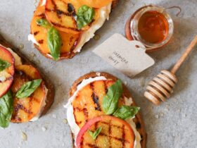 Grilled peach and burrata toast on whole grain bread beautifully plated on rustic wooden board with fresh basil garnish and drizzle of honey