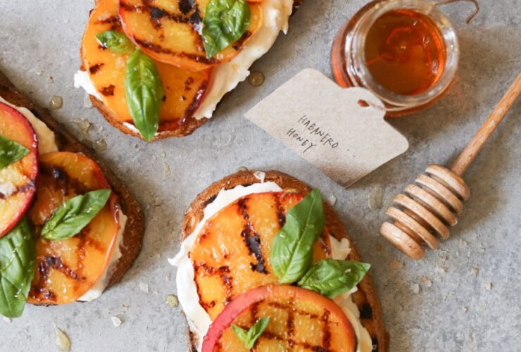 Grilled peach and burrata toast on whole grain bread beautifully plated on rustic wooden board with fresh basil garnish and drizzle of honey