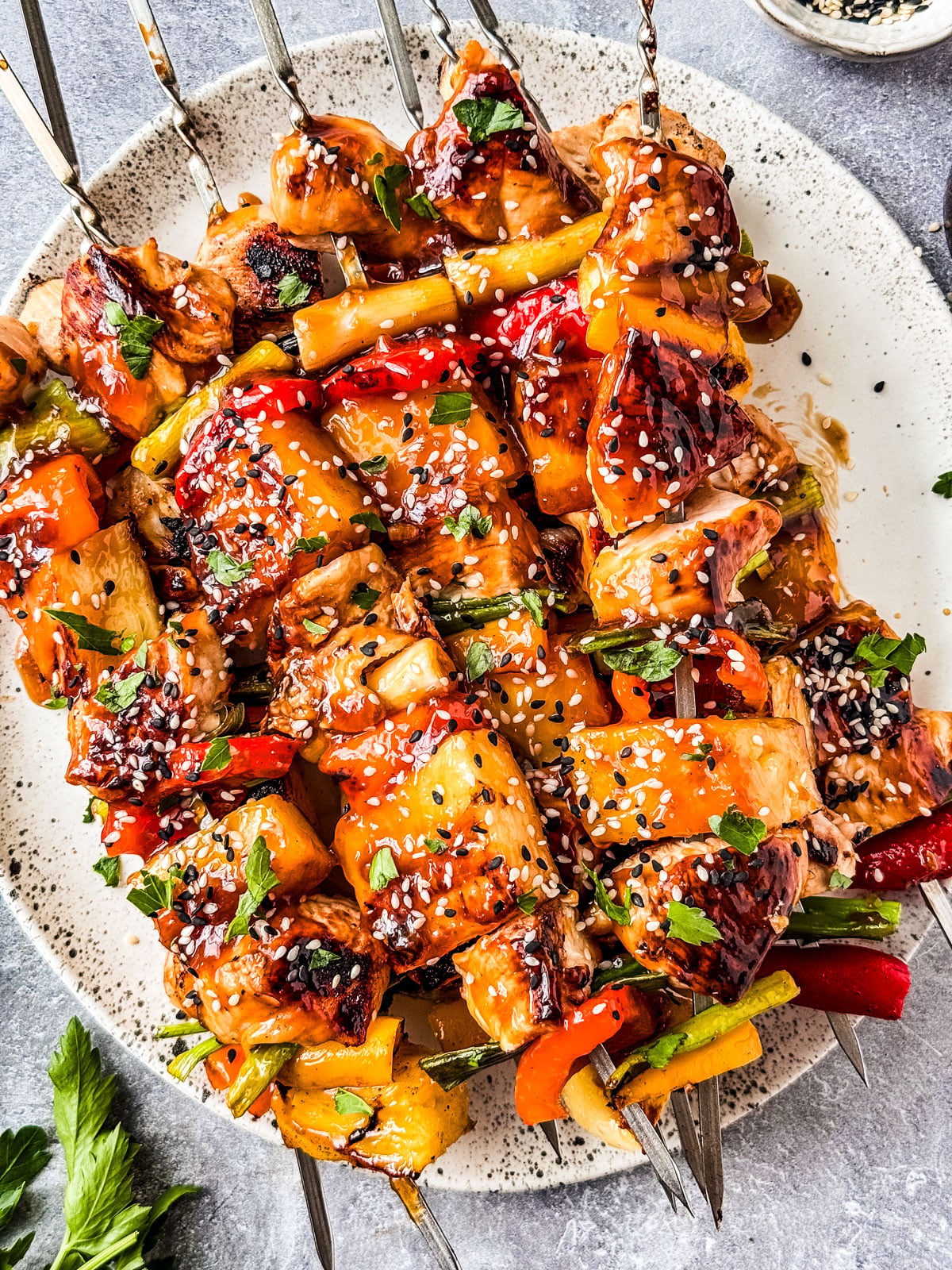 Flat lay ingredients shot showing cubed chicken thighs in marinade, fresh pineapple chunks, colorful bell peppers, red onion, skewers, garlic, ginger, soy sauce, and fresh herbs on a light marble surface