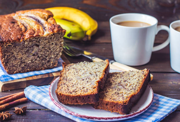 Sliced healthy banana bread on a wooden cutting board with fresh banana slices and a cup of coffee, showing the moist golden interior