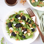 Colorful healthy summer salad with blackberries, spinach, avocado, and walnuts in a white bowl with blackberry balsamic dressing drizzled on top