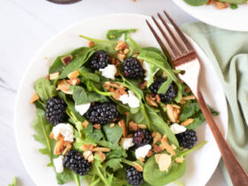 Colorful healthy summer salad with blackberries, spinach, avocado, and walnuts in a white bowl with blackberry balsamic dressing drizzled on top