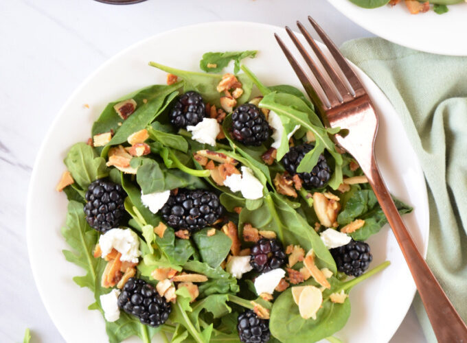Colorful healthy summer salad with blackberries, spinach, avocado, and walnuts in a white bowl with blackberry balsamic dressing drizzled on top
