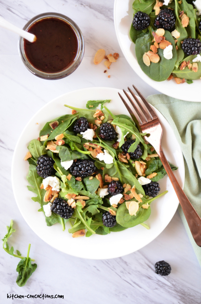 Colorful healthy summer salad with blackberries, spinach, avocado, and walnuts in a white bowl with blackberry balsamic dressing drizzled on top