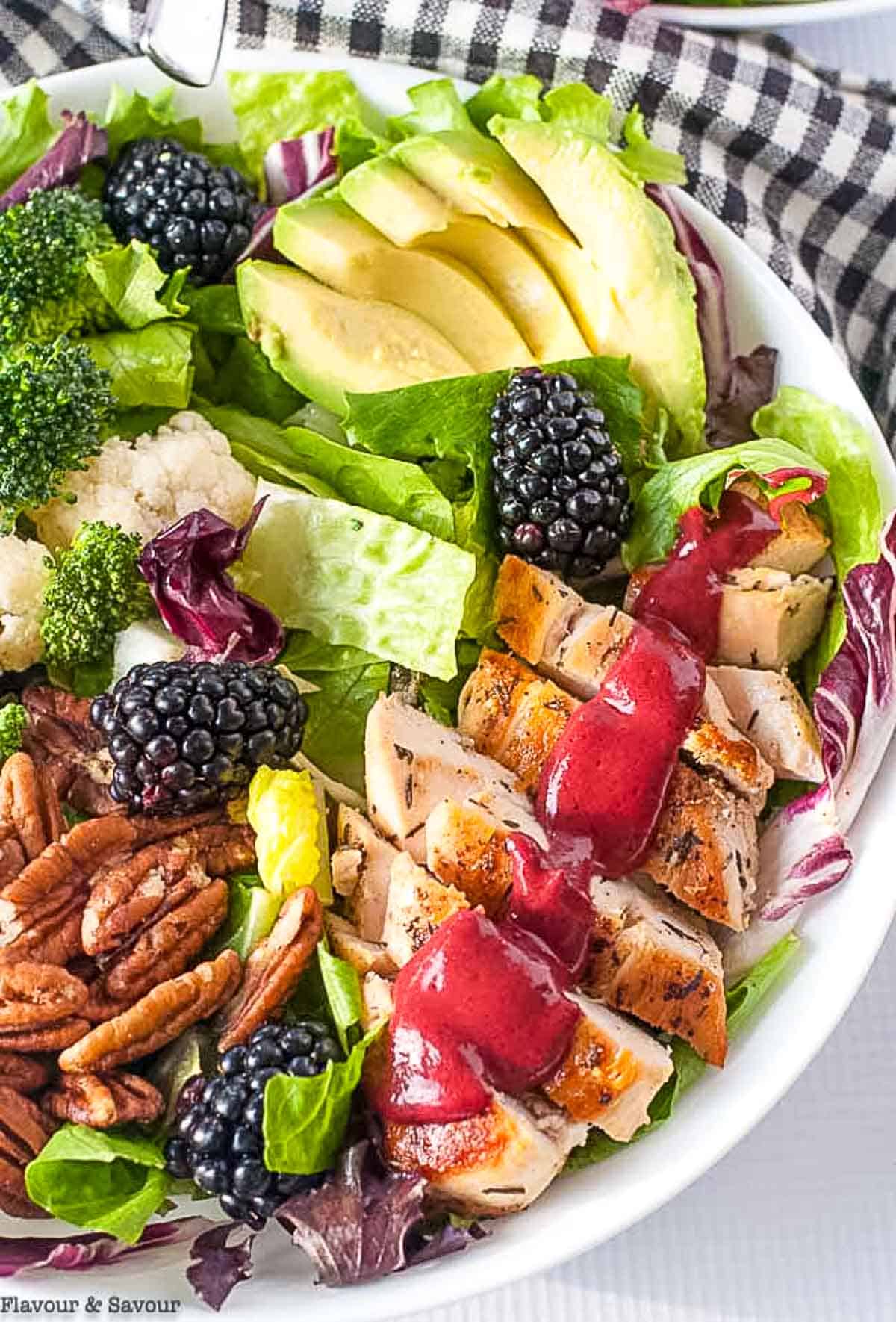 Close-up of healthy summer salad showing glistening blackberries, creamy avocado slices, and crumbled goat cheese with blackberry balsamic dressing