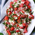 Vibrant watermelon feta mint salad in white ceramic bowl with scattered mint leaves and crumbled feta on marble surface