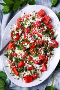 Vibrant watermelon feta mint salad in white ceramic bowl with scattered mint leaves and crumbled feta on marble surface
