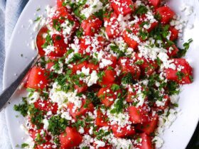 Vibrant watermelon feta mint salad in white ceramic bowl with scattered mint leaves and crumbled feta on marble surface
