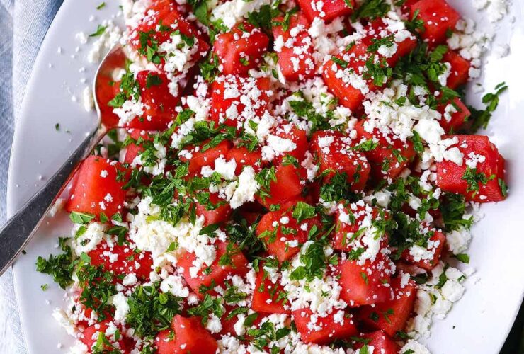 Vibrant watermelon feta mint salad in white ceramic bowl with scattered mint leaves and crumbled feta on marble surface