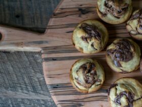 Freshly baked golden cinnamon rolls with cream cheese glaze drizzled on top, arranged on a rustic wooden board with cinnamon sticks and a cup of coffee