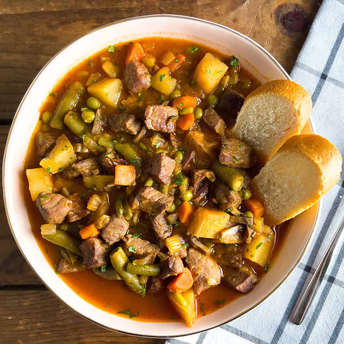 Close-up shot of a spoon lifting tender beef and vegetables from the stew, showing the rich, glossy broth and perfect texture