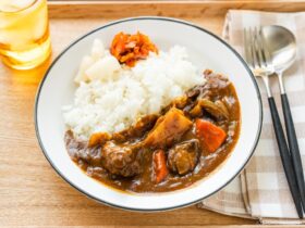 Japanese beef curry served in a white bowl with steamed rice, tender chunks of beef and vegetables visible in rich, golden-brown curry sauce, garnished with fresh herbs