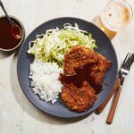 Golden crispy Japanese chicken katsu cutlets plated elegantly with shredded cabbage, steamed rice, and tonkatsu sauce drizzled artistically on white ceramic plates