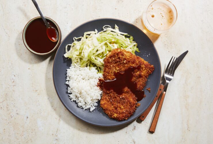 Golden crispy Japanese chicken katsu cutlets plated elegantly with shredded cabbage, steamed rice, and tonkatsu sauce drizzled artistically on white ceramic plates