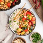 Kung Pao Chicken served in a white bowl with chopsticks, garnished with green onions and crushed peanuts, showing colorful vegetables and tender chicken pieces