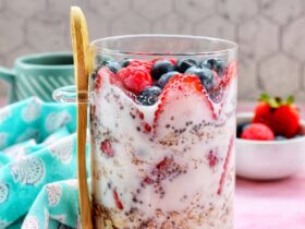 Overnight Oats Summer Berry Recipe — The Ultimate No-Cook Breakfast Jar 36 Overhead shot of two glass mason jars filled with creamy overnight oats, topped with fresh strawberries, blueberries, raspberries, and blackberries, set on a white linen cloth with a wooden spoon and scattered berries around them in warm morning light