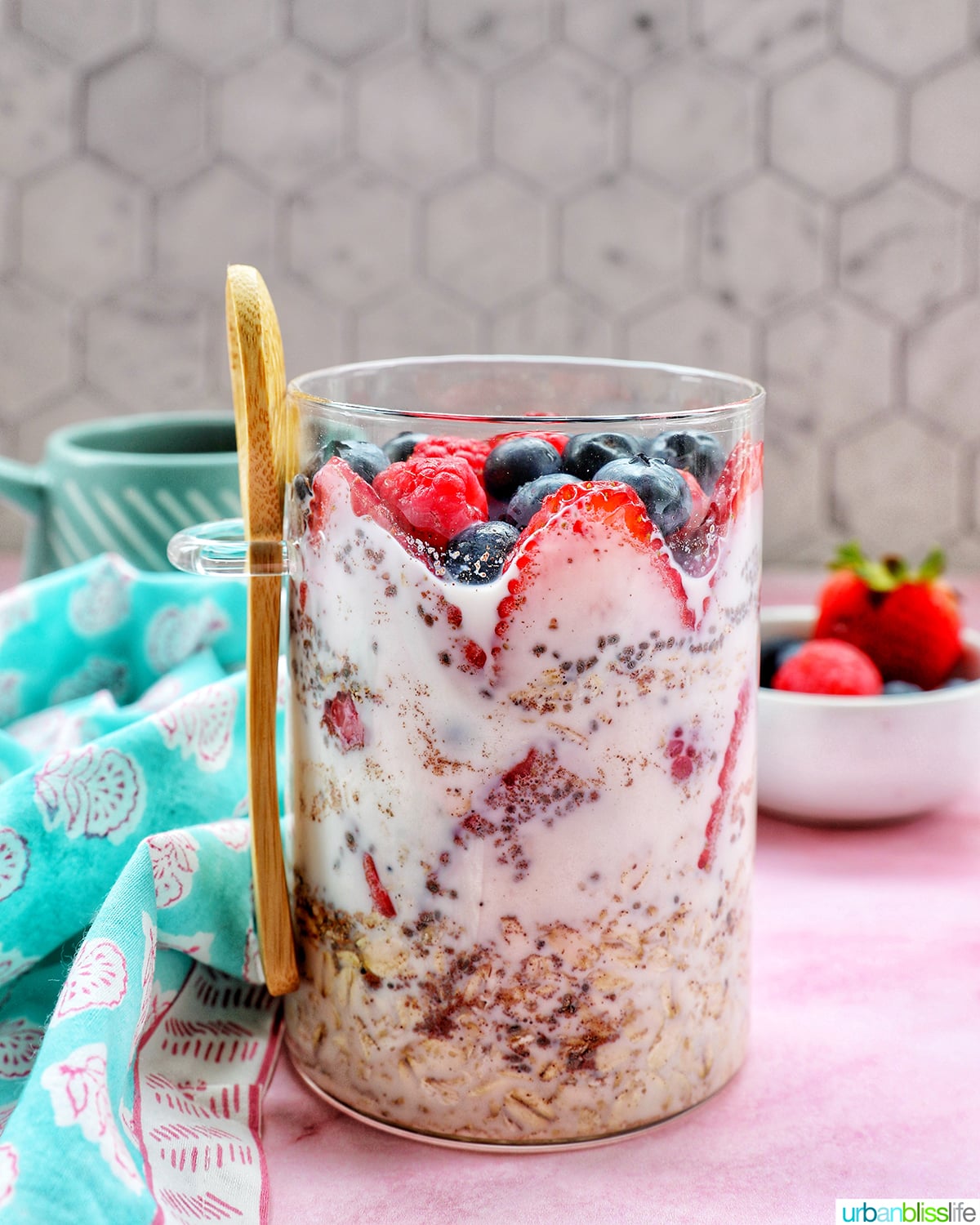 Overnight Oats Summer Berry Recipe — The Ultimate No-Cook Breakfast Jar 26 Overhead shot of two glass mason jars filled with creamy overnight oats, topped with fresh strawberries, blueberries, raspberries, and blackberries, set on a white linen cloth with a wooden spoon and scattered berries around them in warm morning light