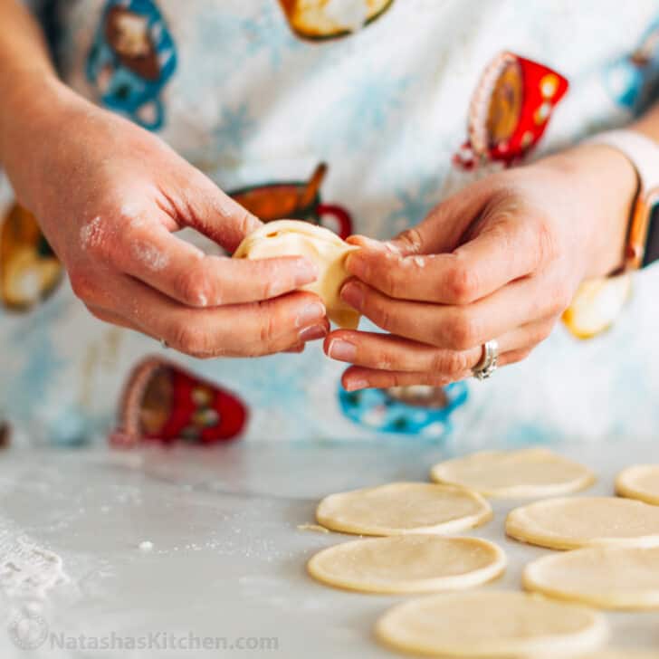 Polish Pierogi Recipe - Authentic European Comfort Food with Nutritious Ingredients 27 Step-by-step shot showing hands crimping pierogi edges with a fork, with rolled dough and filling bowls in the background