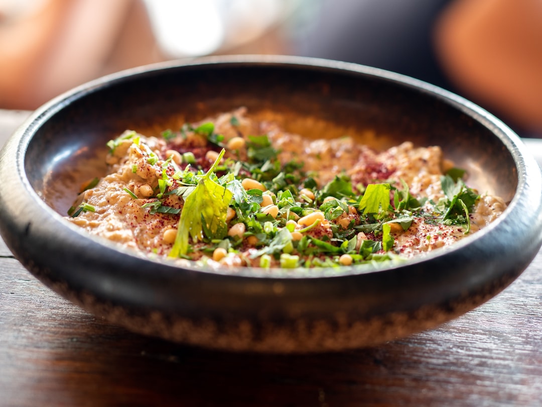 Close-up of a roasted chickpea hummus bowl served in a white ceramic bowl, showing the texture of crispy golden chickpeas, vibrant fresh vegetables, and a drizzle of olive oil and fresh herbs