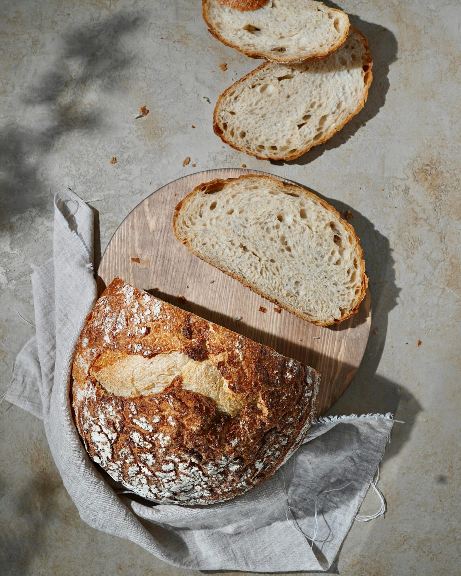 Golden brown sourdough bread loaf with perfectly crispy crust and airy crumb, artfully placed on rustic wooden cutting board with wheat stalks