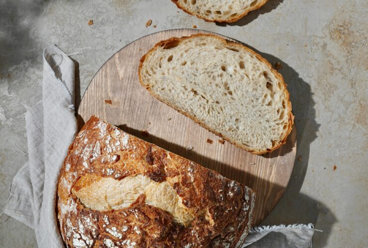 Golden brown sourdough bread loaf with perfectly crispy crust and airy crumb, artfully placed on rustic wooden cutting board with wheat stalks