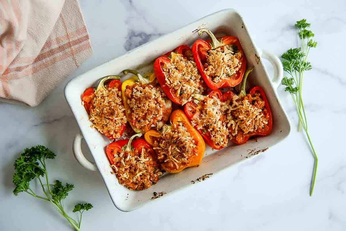 Overhead flat-lay of raw bell peppers halved and hollowed out, bowls of cooked quinoa, seasoned ground turkey, diced tomatoes, fresh herbs, and crumbled feta arranged on a wooden prep surface
