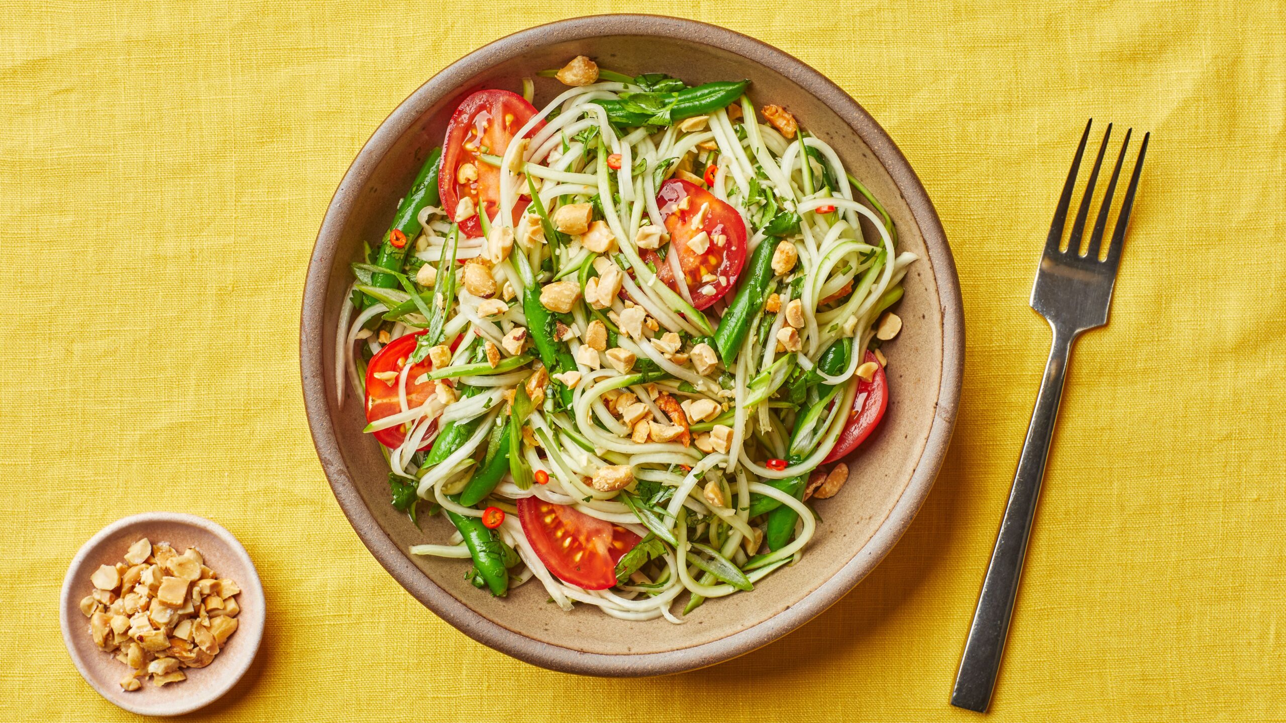 Flat-lay ingredients shot for healthy Thai papaya salad som tam showing shredded green papaya, halved cherry tomatoes, sliced bird's eye chilies, lime wedges, fish sauce, palm sugar, garlic cloves, long beans, and roasted peanuts arranged on a white marble surface