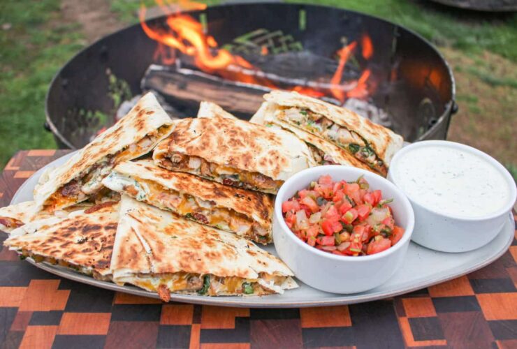 Campfire Quesadillas — Crispy 2-Ingredient Skillet Magic You'll Make All Summer 36 Golden crispy campfire quesadillas served on a rustic wooden board outdoors near a campfire, cut into wedges with melted cheese pulling apart