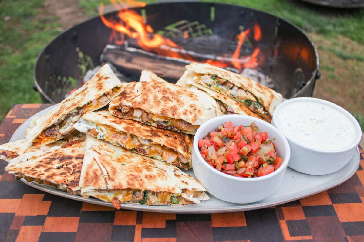 Campfire Quesadillas — Crispy 2-Ingredient Skillet Magic You'll Make All Summer 26 Golden crispy campfire quesadillas served on a rustic wooden board outdoors near a campfire, cut into wedges with melted cheese pulling apart