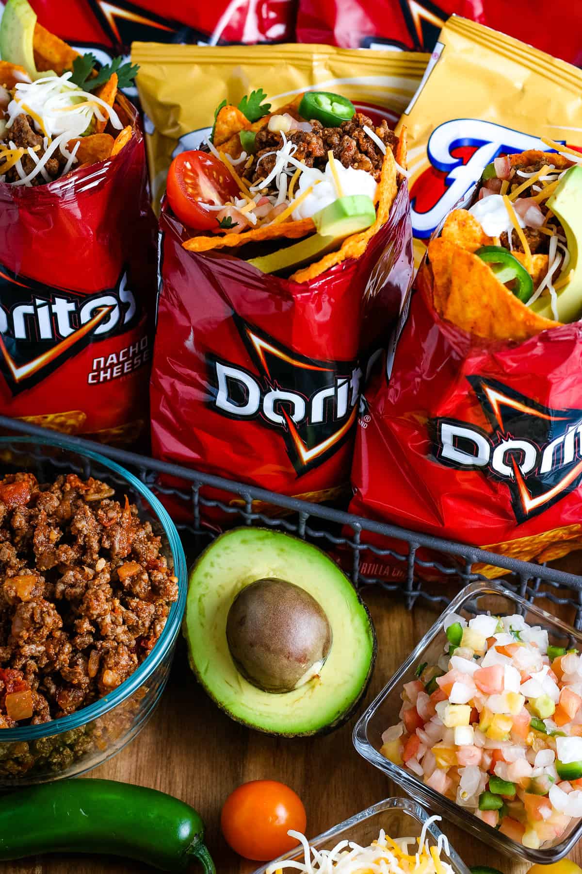 Campfire Walking Tacos — Easy Dorito Bag Tacos with Seasoned Beef & All the Toppings 26 Campfire walking tacos served in open Dorito bags with seasoned beef, shredded cheese, sour cream, salsa, and fresh toppings on a rustic wooden camp table beside a glowing campfire at dusk