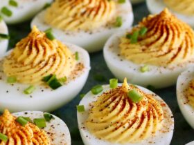 Classic deviled eggs arranged on a white ceramic serving platter, topped with smoked paprika and fresh chives, shot from above on a rustic wooden picnic table