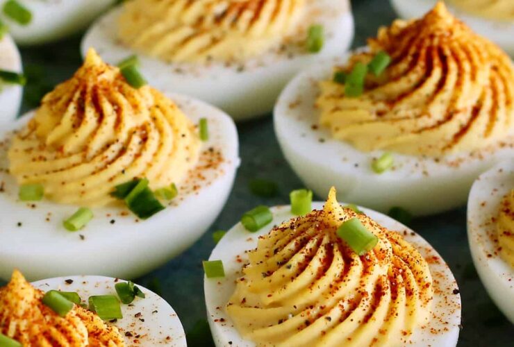Classic deviled eggs arranged on a white ceramic serving platter, topped with smoked paprika and fresh chives, shot from above on a rustic wooden picnic table