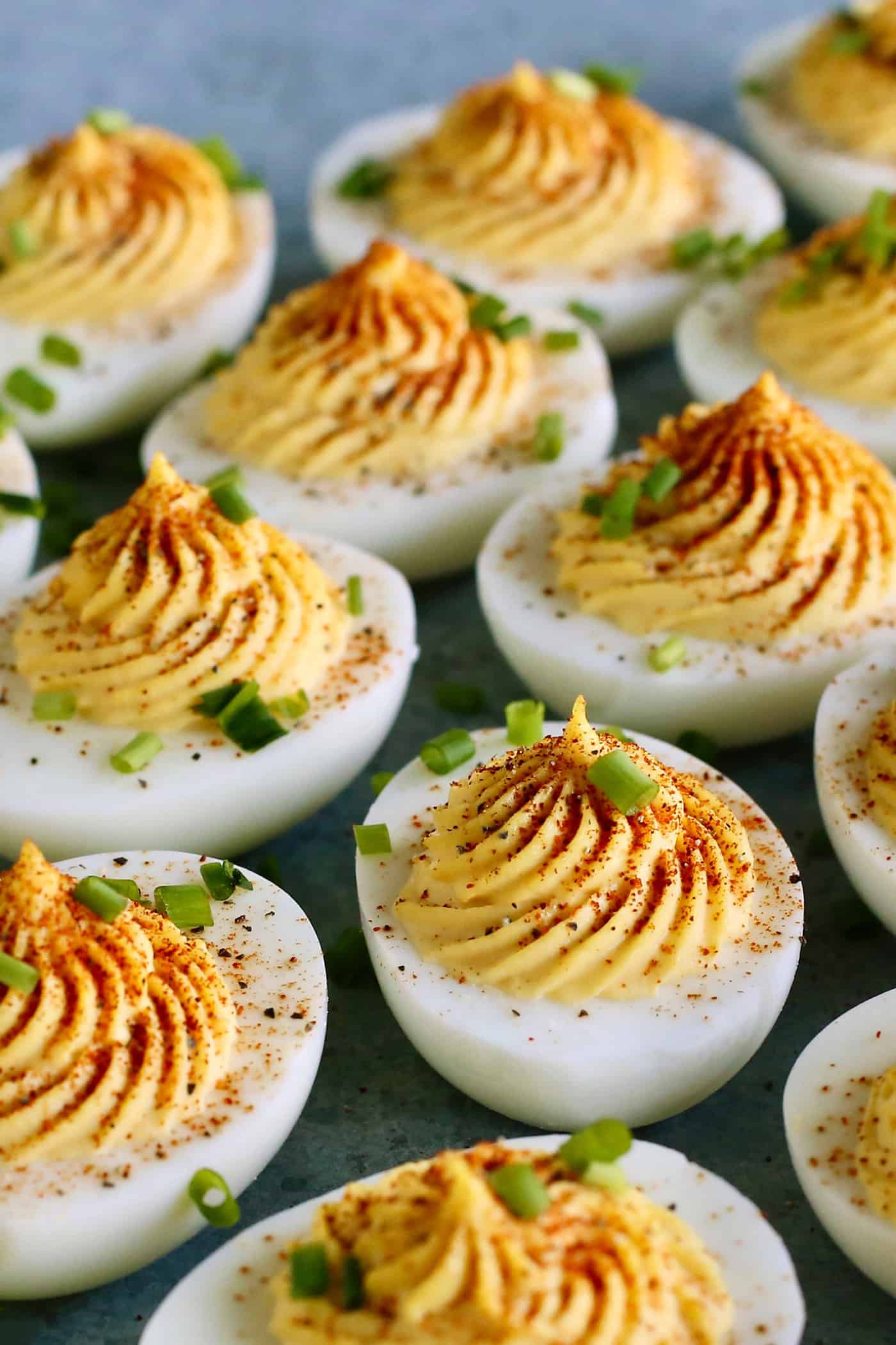 Classic Deviled Eggs — Paprika Dusted Picnic Appetizer Everyone Loves 26 Classic deviled eggs arranged on a white ceramic serving platter, topped with smoked paprika and fresh chives, shot from above on a rustic wooden picnic table