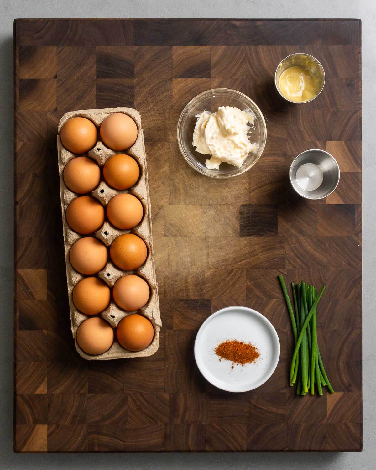 Classic Deviled Eggs — Paprika Dusted Picnic Appetizer Everyone Loves 27 Step-by-step flat lay of deviled egg ingredients — hard boiled eggs halved on a cutting board, a small bowl of creamy yolk filling, smoked paprika in a spoon, and a piping bag, shot from above on a white marble surface